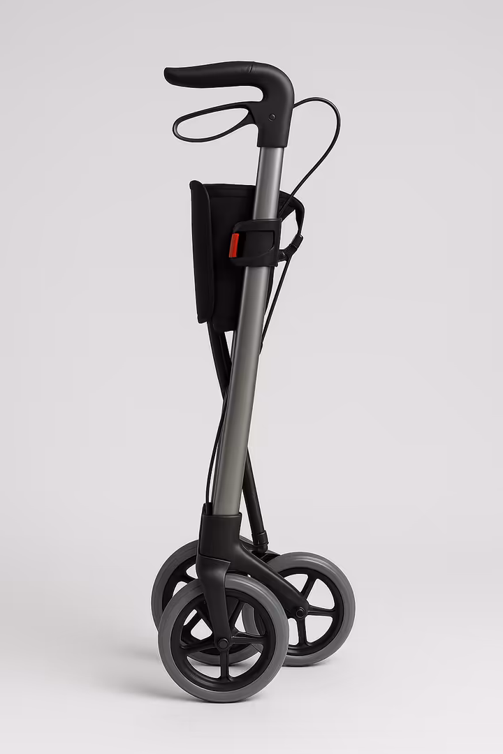 A narrow Euro-style rollator folded side-to-side, standing on its own in a compact form.