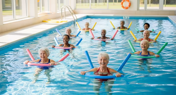 A group of happy seniors participating in a water aerobics class with colorful pool noodles.