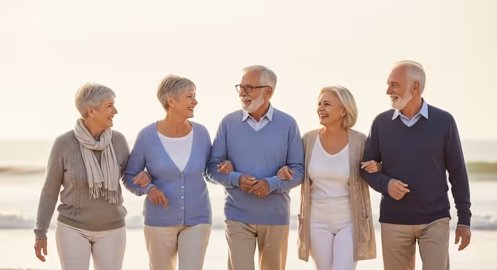 A diverse group of three seniors walking together on the beach, smiling and talking.