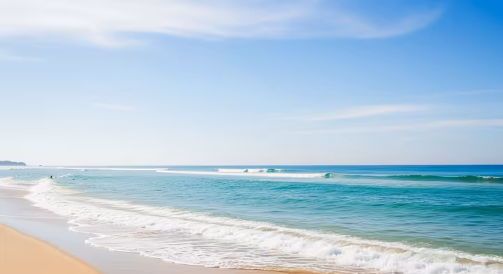 A tranquil view of the ocean meeting the beach under a clear blue sky, illustrating a calming 'Blue Space'.